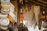 A market stall displays various handmade crafts, including woven baskets, intricate macram&eacute; wall hangings, and embroidered hats. The setting is rustic, with wooden beams and ambient lighting, creating a cozy and artisanal atmosphere.