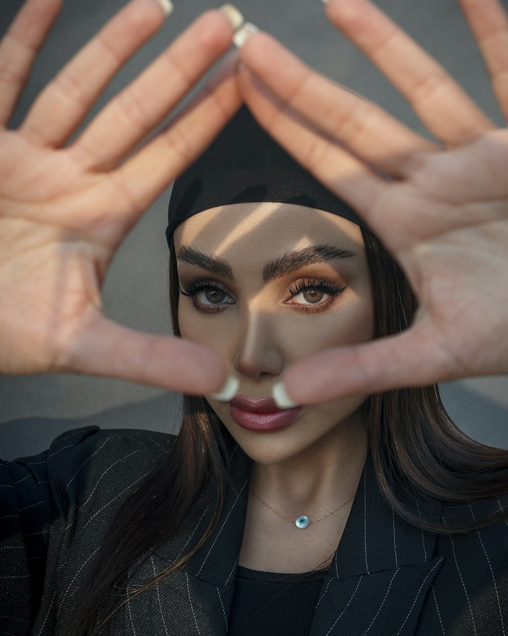 a woman wearing a black hat and holding her hands up to her face