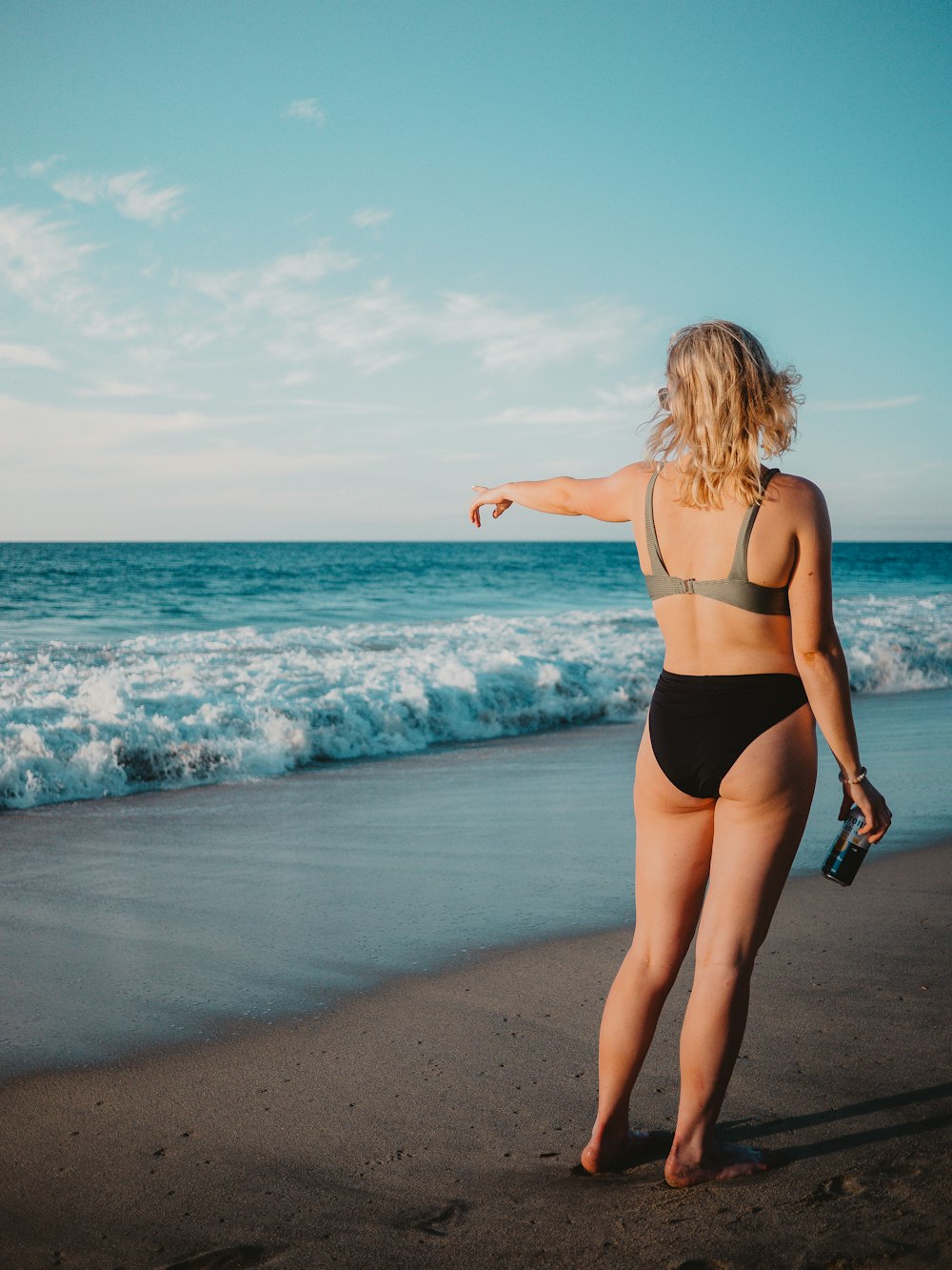 a woman in a bikini pointing at the ocean