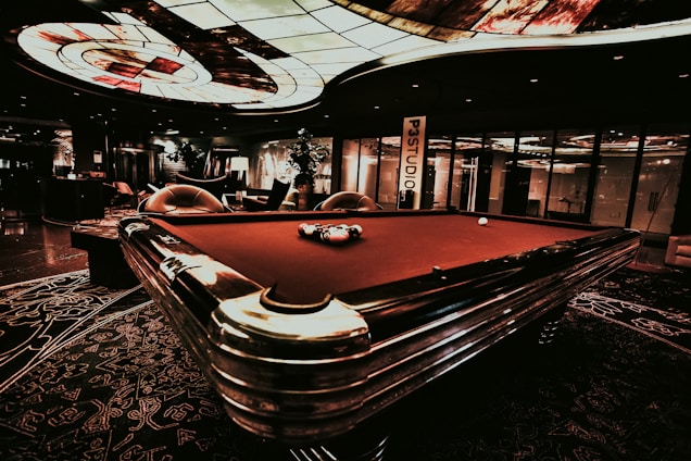 Luxurious casino interior with green billiard cloth, red velvet seats, and golden metallic accents under soft lighting.