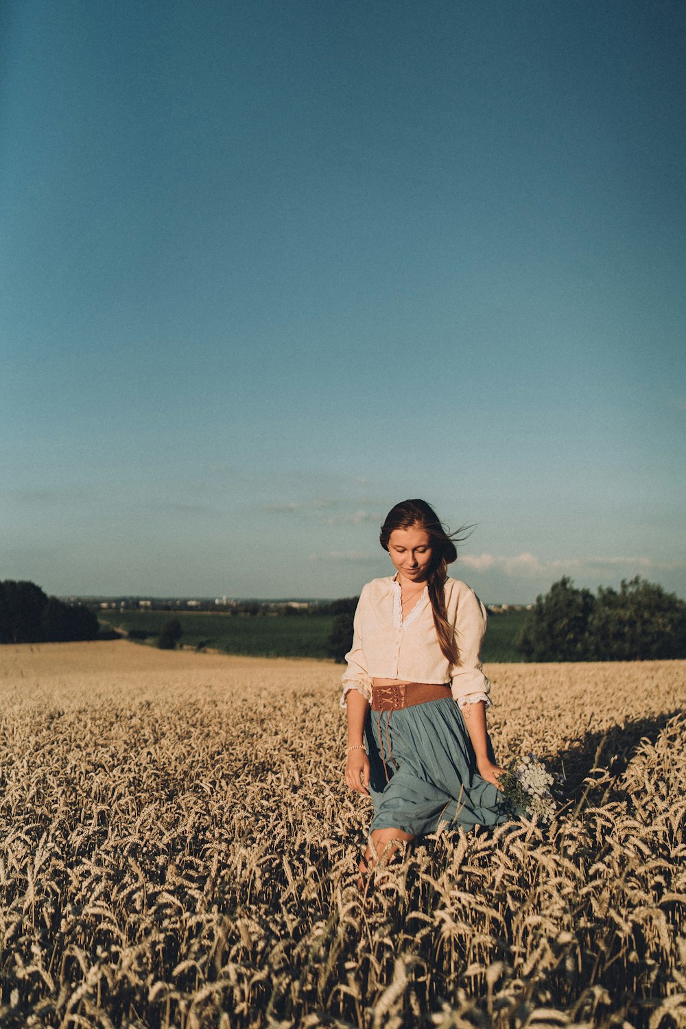 a woman kneeling in a field of wheat