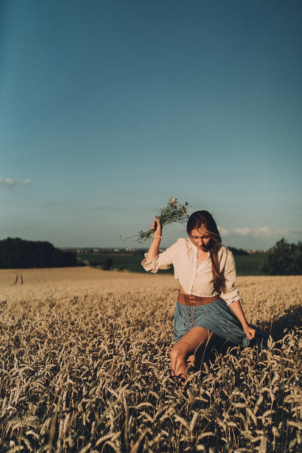 a woman kneeling in a field holding a plant