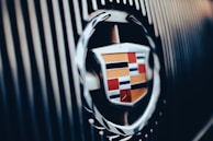 A close-up view of a Cadillac emblem, prominently displayed with metallic edging and colorful shield design, set against a background of vertical lines.