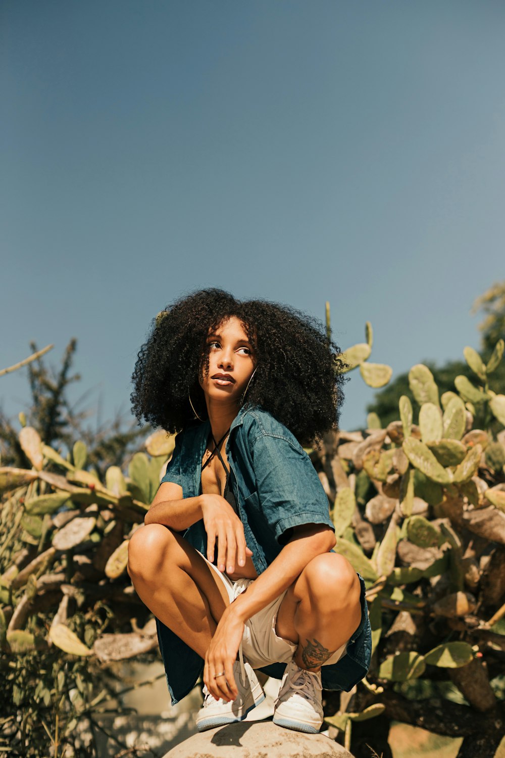 a woman sitting on top of a rock next to a cactus