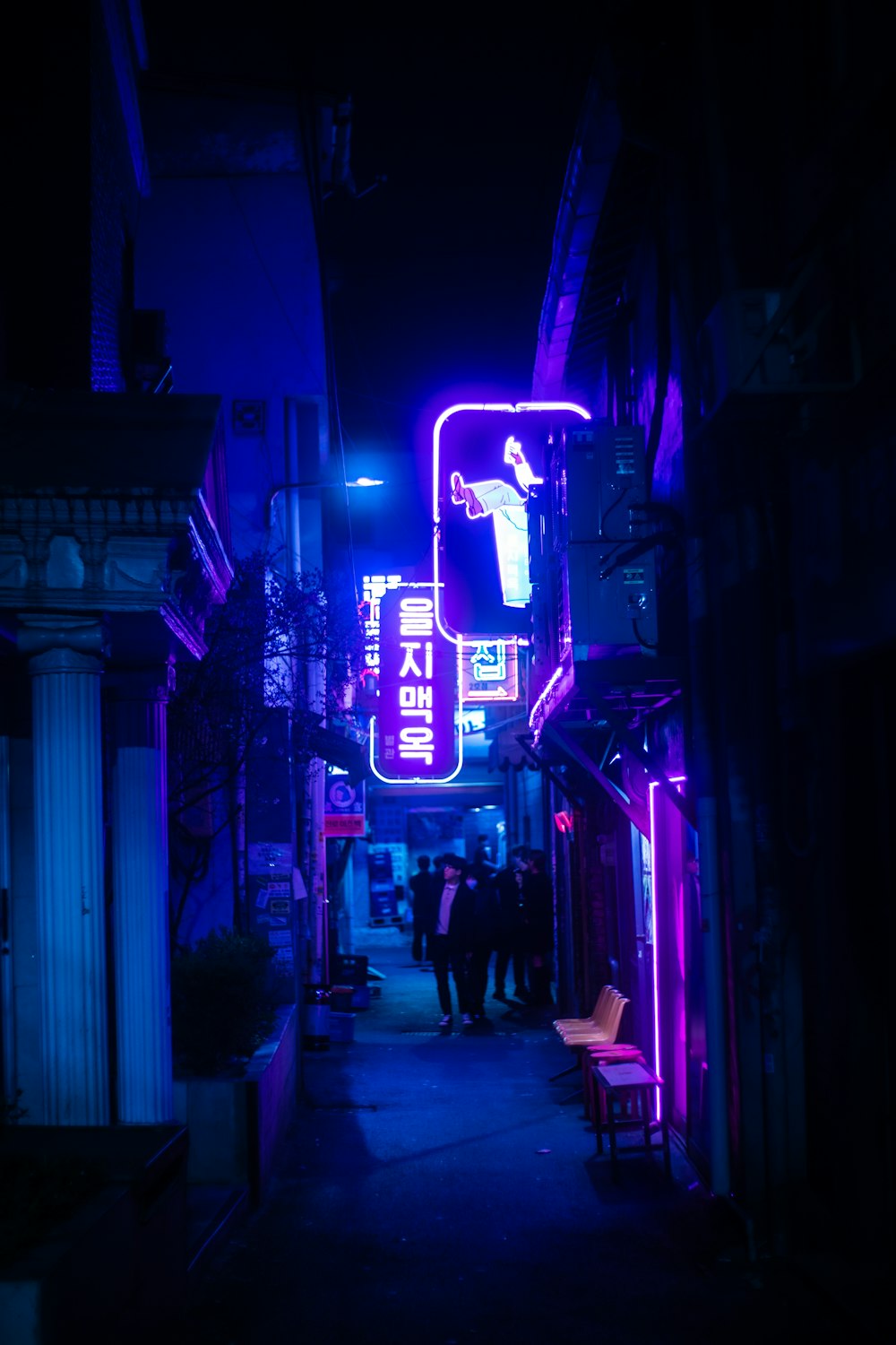 a dark alley with neon signs and people walking down it