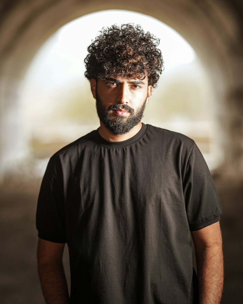 a man with curly hair and beard standing in a tunnel