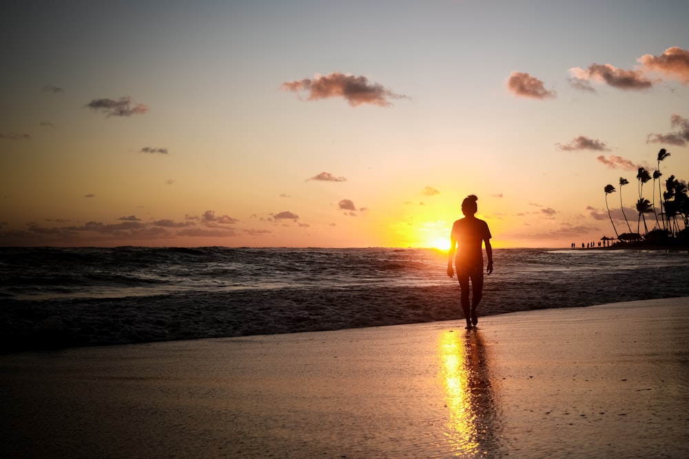 a man walking on the beach at sunset