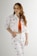 A person with long, wavy brown hair is posing confidently while wearing a matching white denim jacket and pants set adorned with colorful lip prints. They are also wearing an orange top underneath the jacket.
