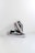 A pair of black sneakers with white soles and a distinctive white side stripe, set against a minimalistic white background. One shoe is positioned upright, resting against the other, showcasing the brown waffle-patterned outsole.