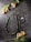 A handcrafted necklace with intricate beadwork and metal detailing lies on a textured stone surface. Surrounding the necklace are delicate yellow and pink flowers with long green stems and leaves. The overall appearance is both rustic and elegant, blending natural elements with artisan jewelry.