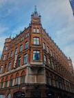 A historic multi-story brick building with ornate architectural details, including arched windows and decorative spires. The sign on the side reveals it to be a hotel. The sky is partially cloudy, suggesting a cool atmosphere.