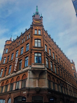 A historic multi-story brick building with ornate architectural details, including arched windows and decorative spires. The sign on the side reveals it to be a hotel. The sky is partially cloudy, suggesting a cool atmosphere.