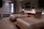 A modern hotel room features two neatly made double beds with striped pillows and runners. The room has a minimalist design with neutral tones, decorated with framed pictures and wall-mounted lights above the beds. A small seating area by a large window adds to the comfortable atmosphere.