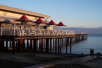 a pier with red umbrellas and people sitting on it