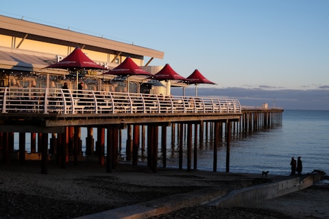 a pier with red umbrellas and people sitting on it