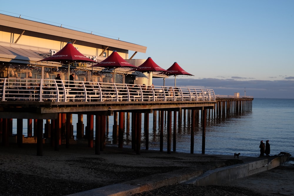 a pier with red umbrellas and people sitting on it