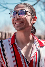 A close-up of a person wearing stylish twinsight glasses, smiling under natural sunlight.