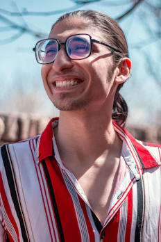 A person wearing classic round eyeglasses, smiling under bright daylight.