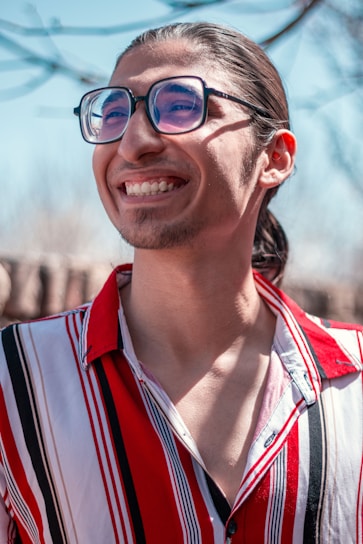 Stylish person wearing classic teyes eyeglasses, smiling confidently outdoors on a sunny day.