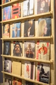 A display shelf filled with vinyl records, each showcasing album artwork. The records are neatly organized on wooden shelves, and the covers feature various artists and designs, ranging from portraits to abstract art.