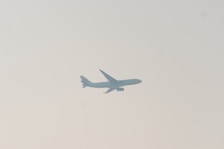 A commercial airplane is silhouetted against a pale sky, with its wings and tail clearly visible. The image conveys a sense of movement and travel.