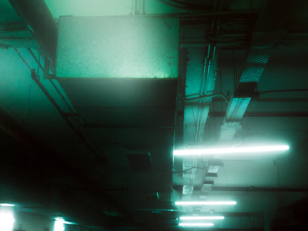 A flickering fluorescent light overhead casts eerie shadows on rusted pipes and dripping concrete walls.