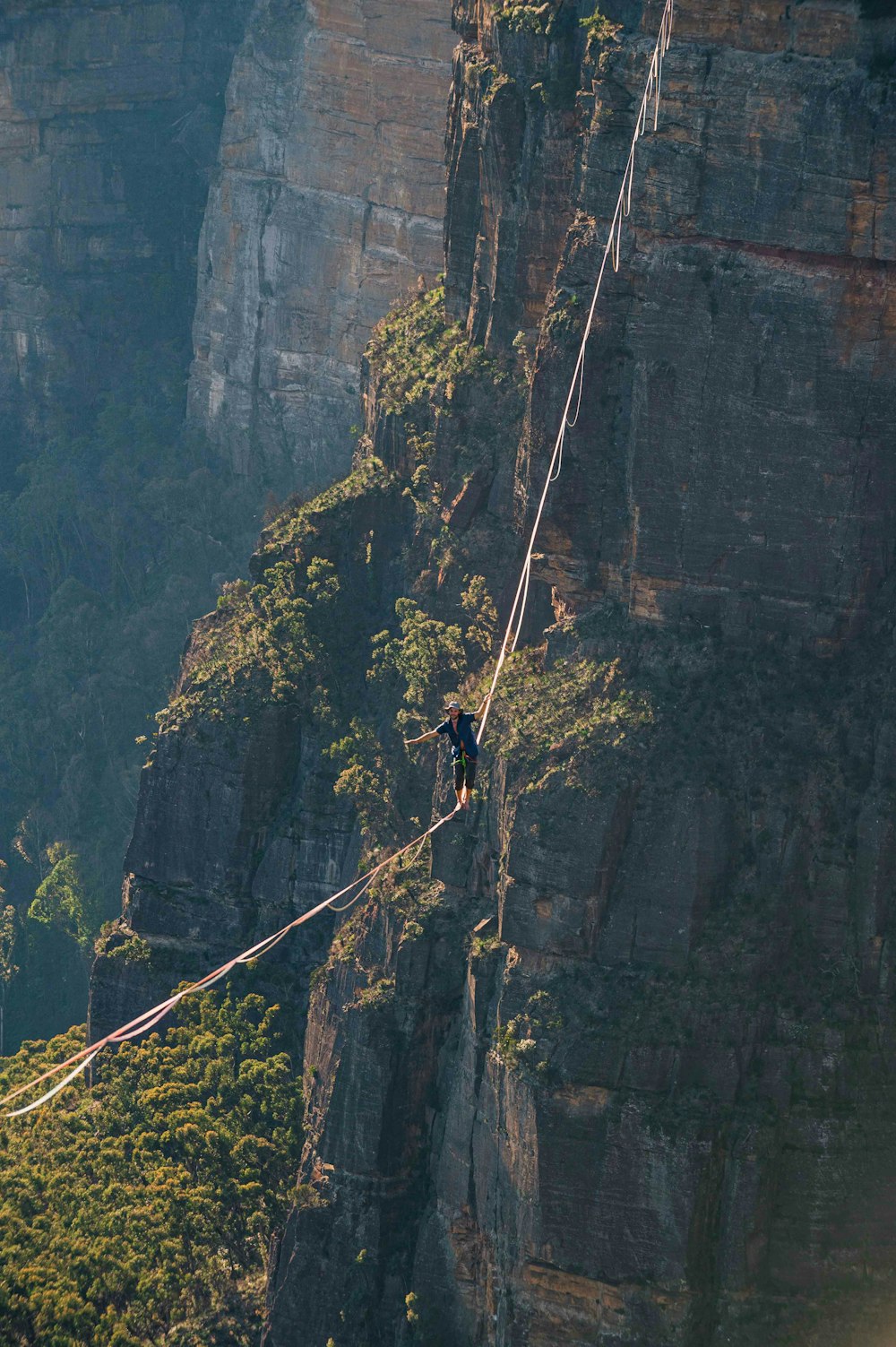 a man walking across a rope on top of a mountain