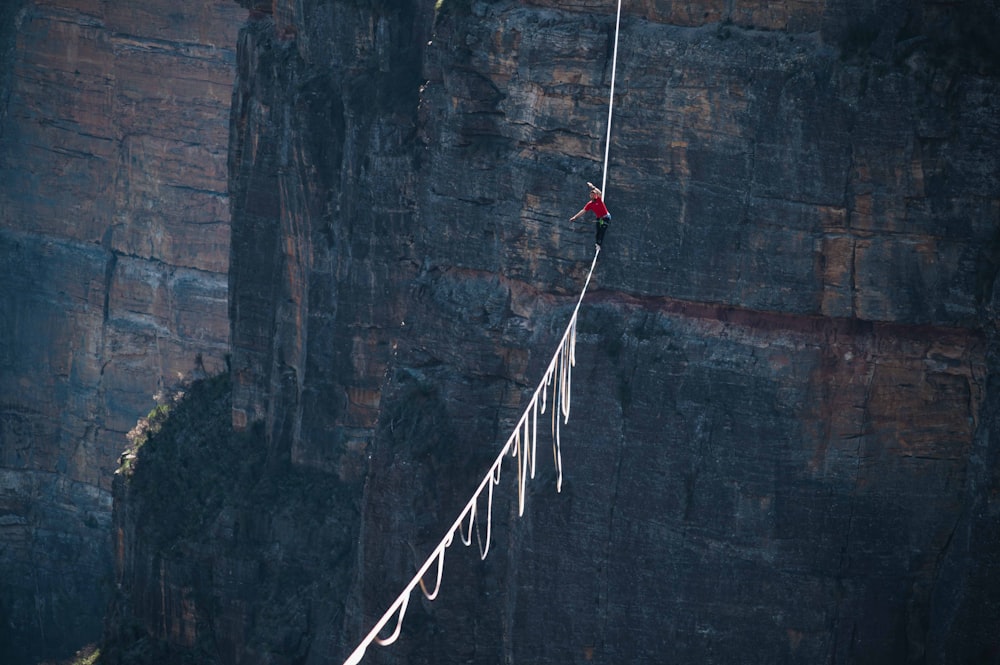 a man walking across a rope on top of a cliff