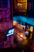 A dark alley scene with subtle hints of deep red neon lights reflecting on wet pavement.