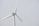 A wind turbine with large white blades set against a pale sky. The turbine has a company logo on the central hub.