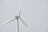 A wind turbine with large white blades set against a pale sky. The turbine has a company logo on the central hub.