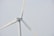 A wind turbine with large white blades set against a pale sky. The turbine has a company logo on the central hub.