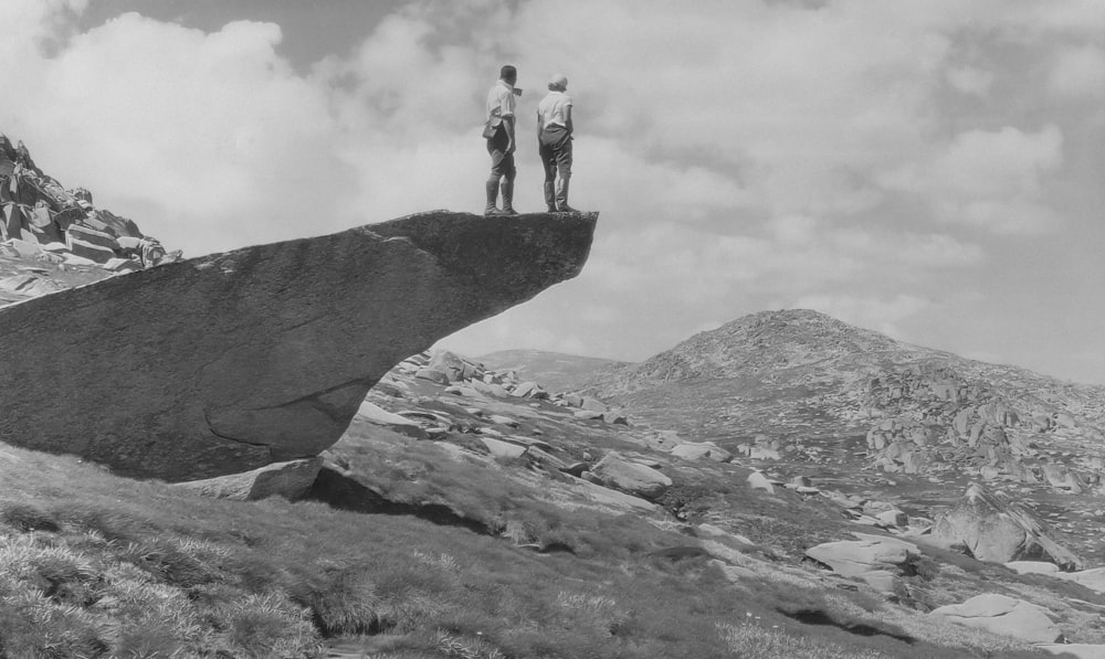 two people standing on top of a large rock