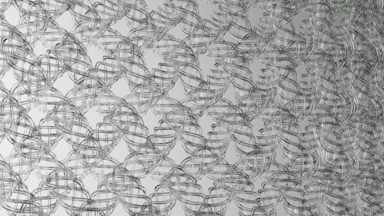 Interwoven metallic wireframes create a lattice-like pattern. The cables form a complex, repeating geometric structure, giving the impression of a mesh or net. The overall design is symmetrical and organized, producing a three-dimensional visual effect.