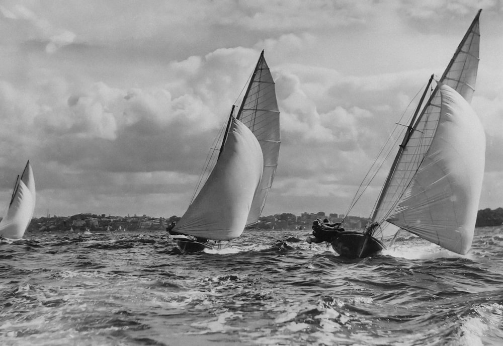 a black and white photo of three sailboats in the ocean