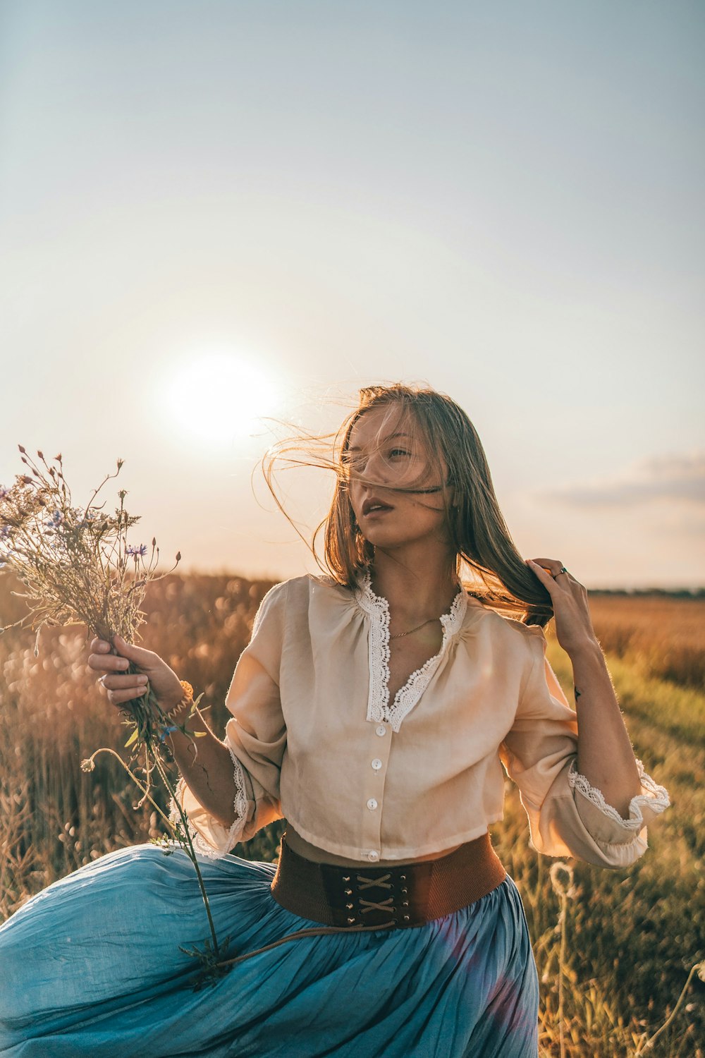 a woman sitting in a field holding a bunch of flowers