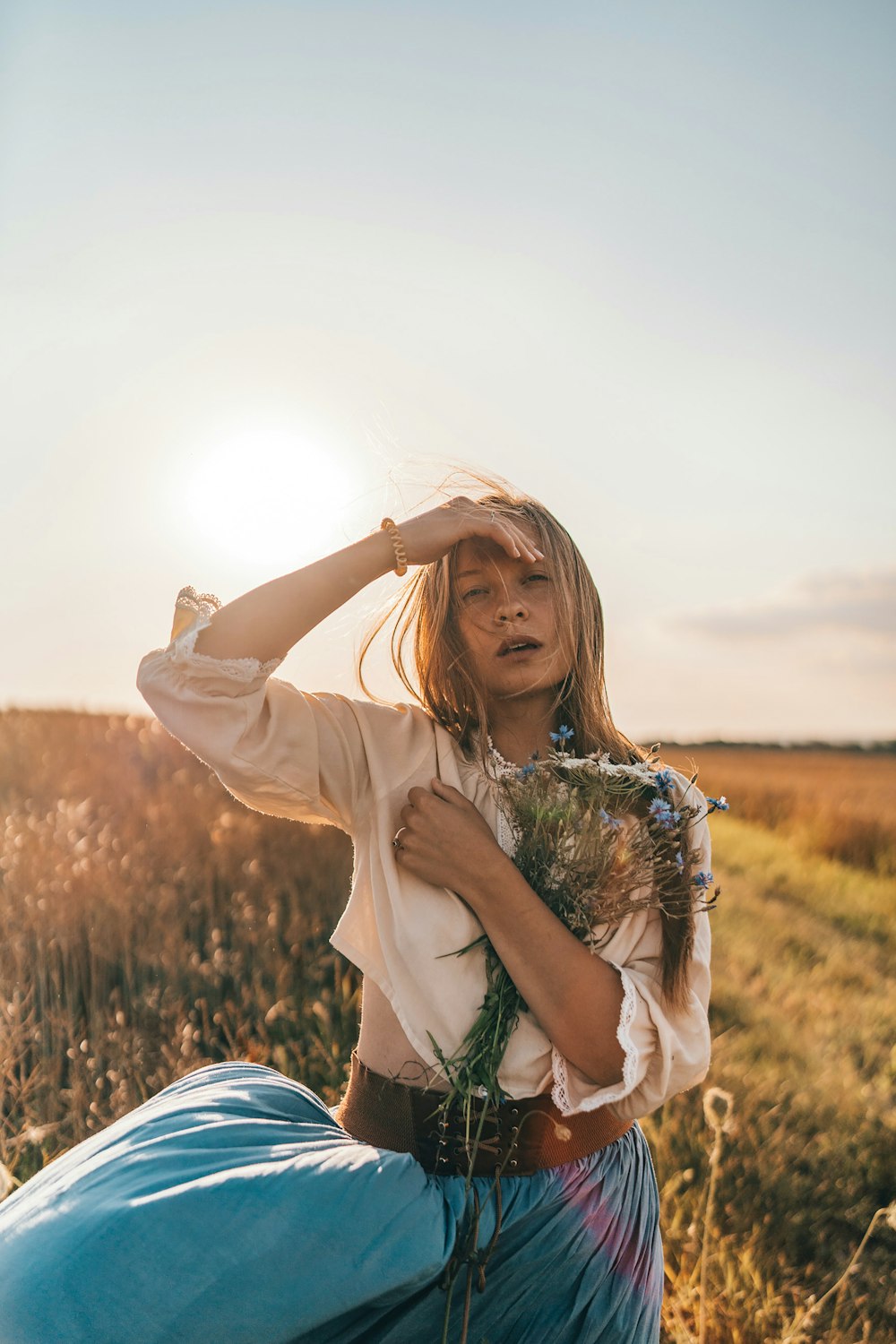 a woman sitting in a field holding a bouquet of flowers