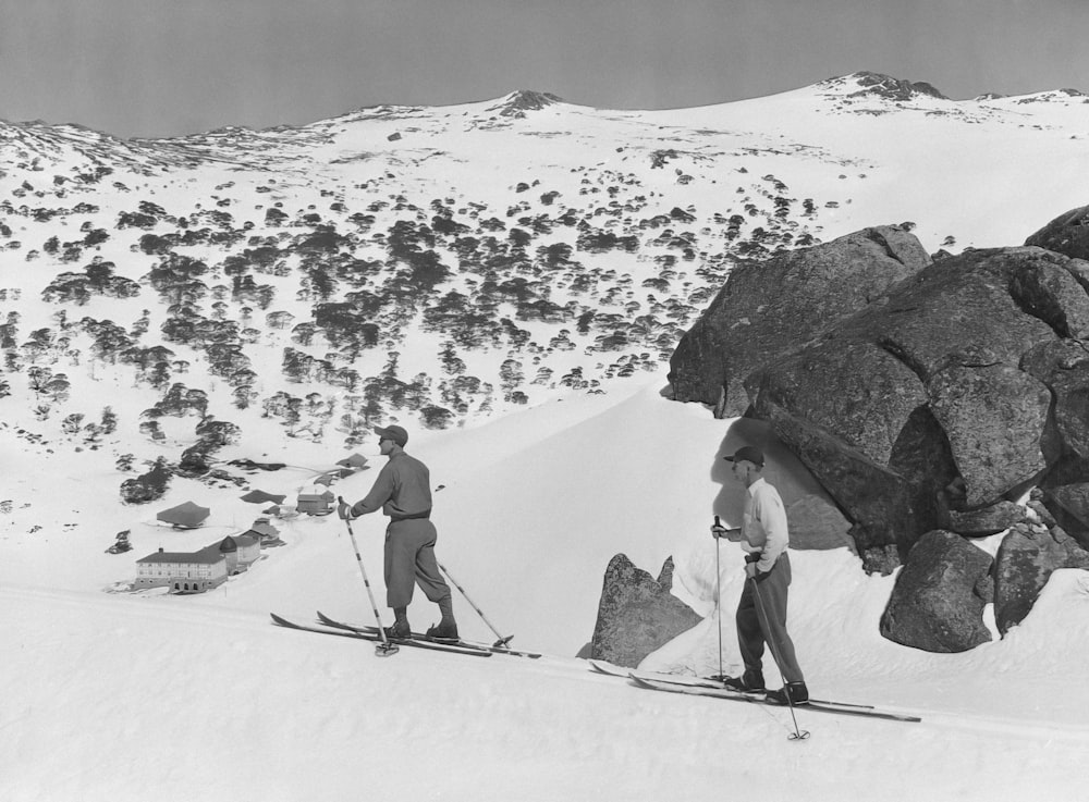 a couple of men riding skis down a snow covered slope