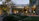 A modern architectural setting with large glass windows reflecting a softly lit interior. The foreground features a lush garden with various trees, shrubs, and rocks. There's a patio area with comfortable seating next to a small water feature, creating a serene outdoor living space.