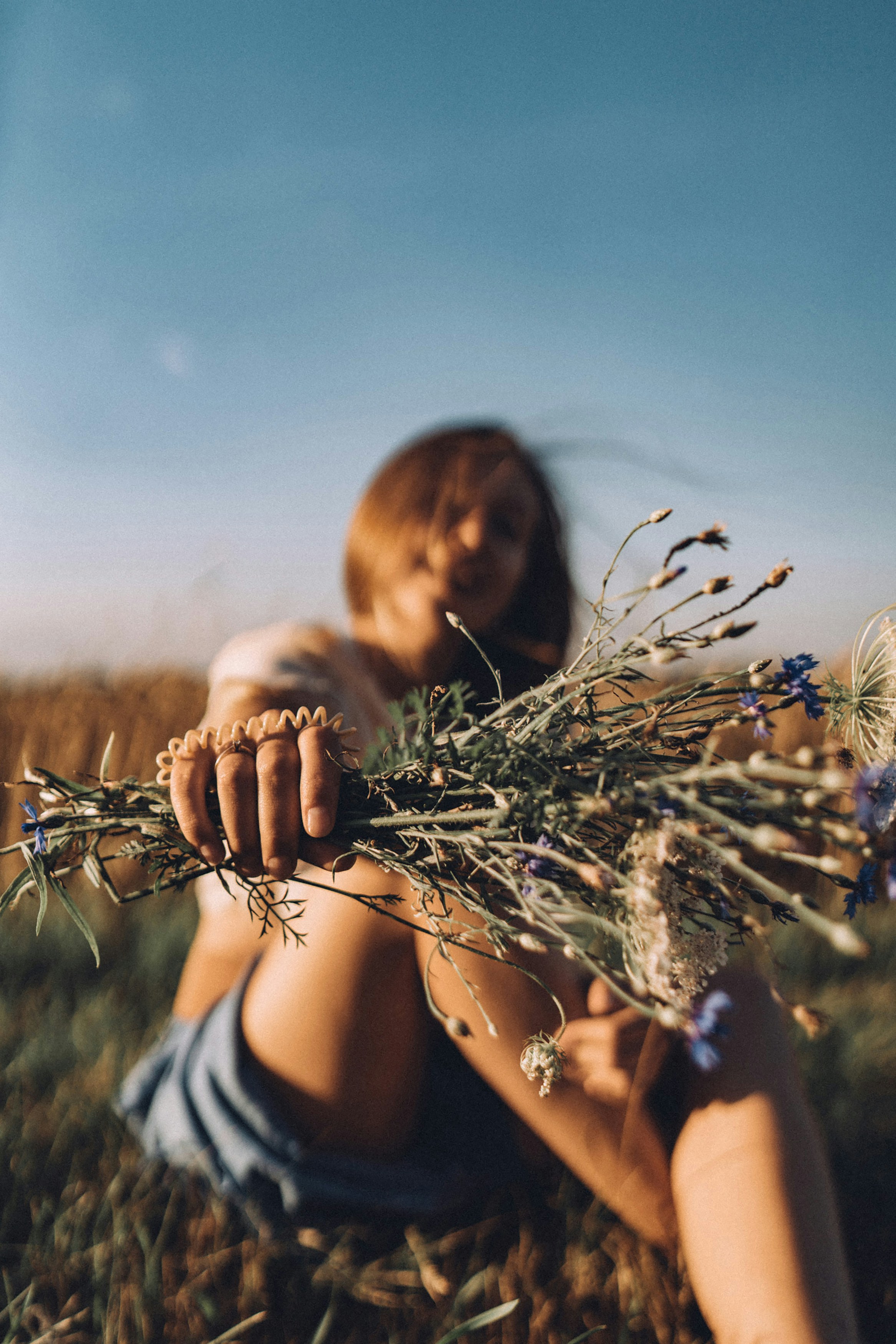 a woman sitting in a field holding a bunch of flowers