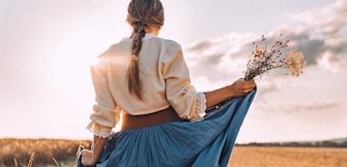 a woman standing in a field holding a bouquet of flowers