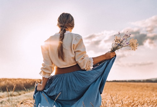 a woman standing in a field holding a bouquet of flowers