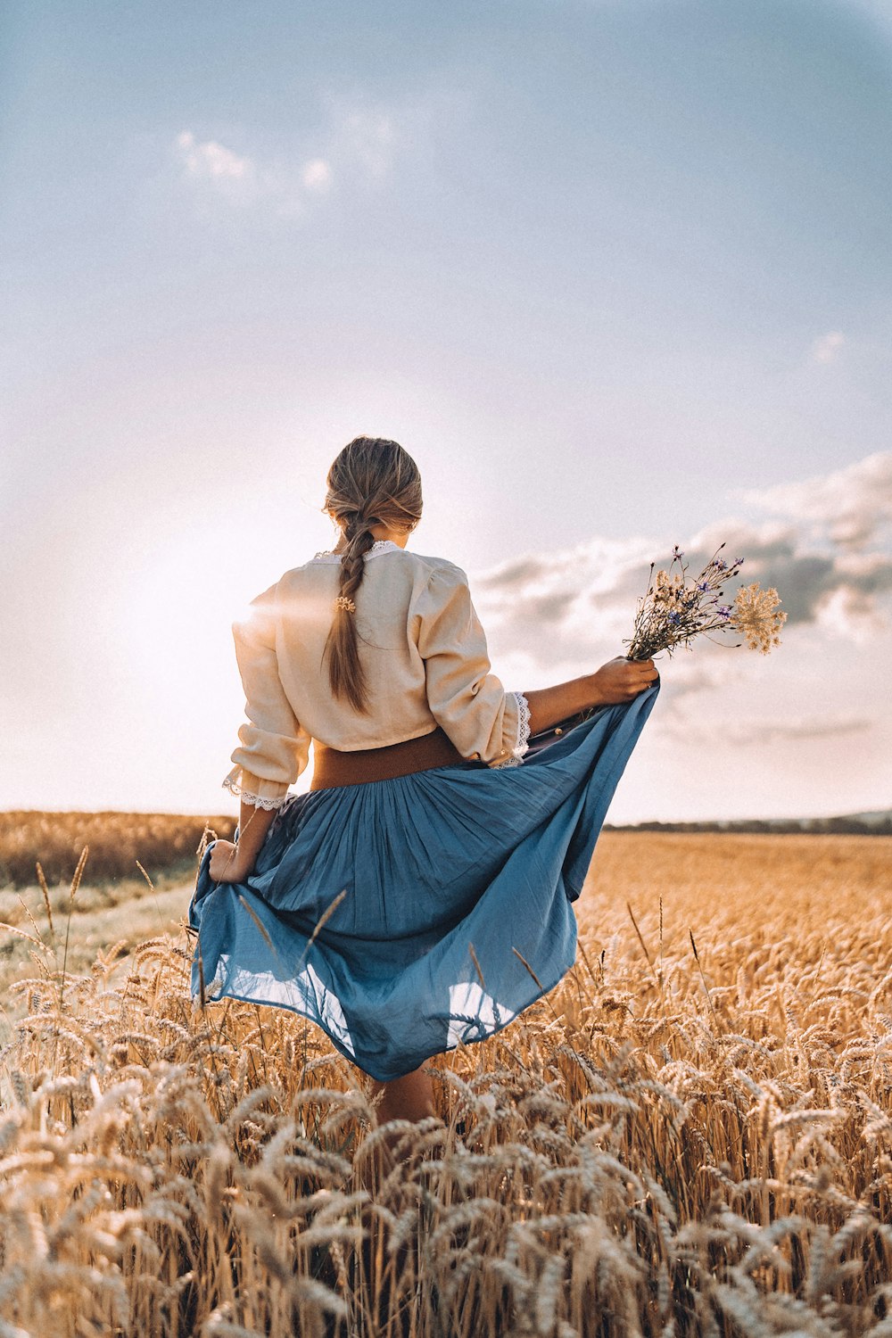 a woman standing in a field holding a bouquet of flowers