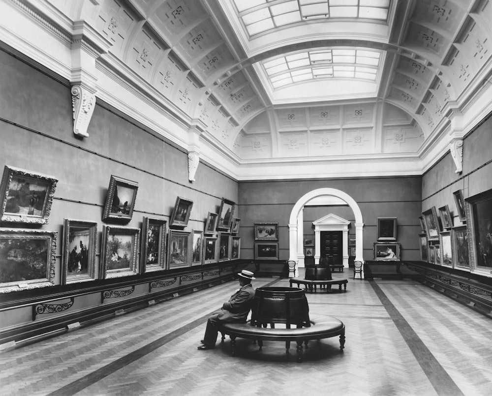 a black and white photo of a person sitting on a bench in a museum