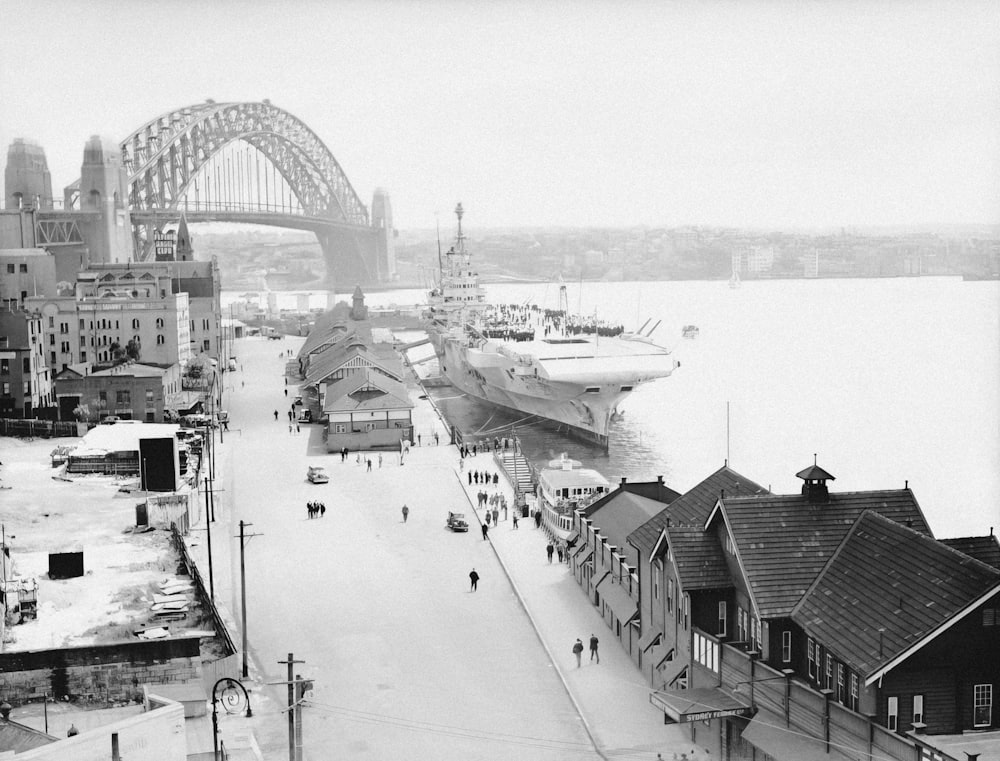 a black and white photo of a harbor with a bridge in the background