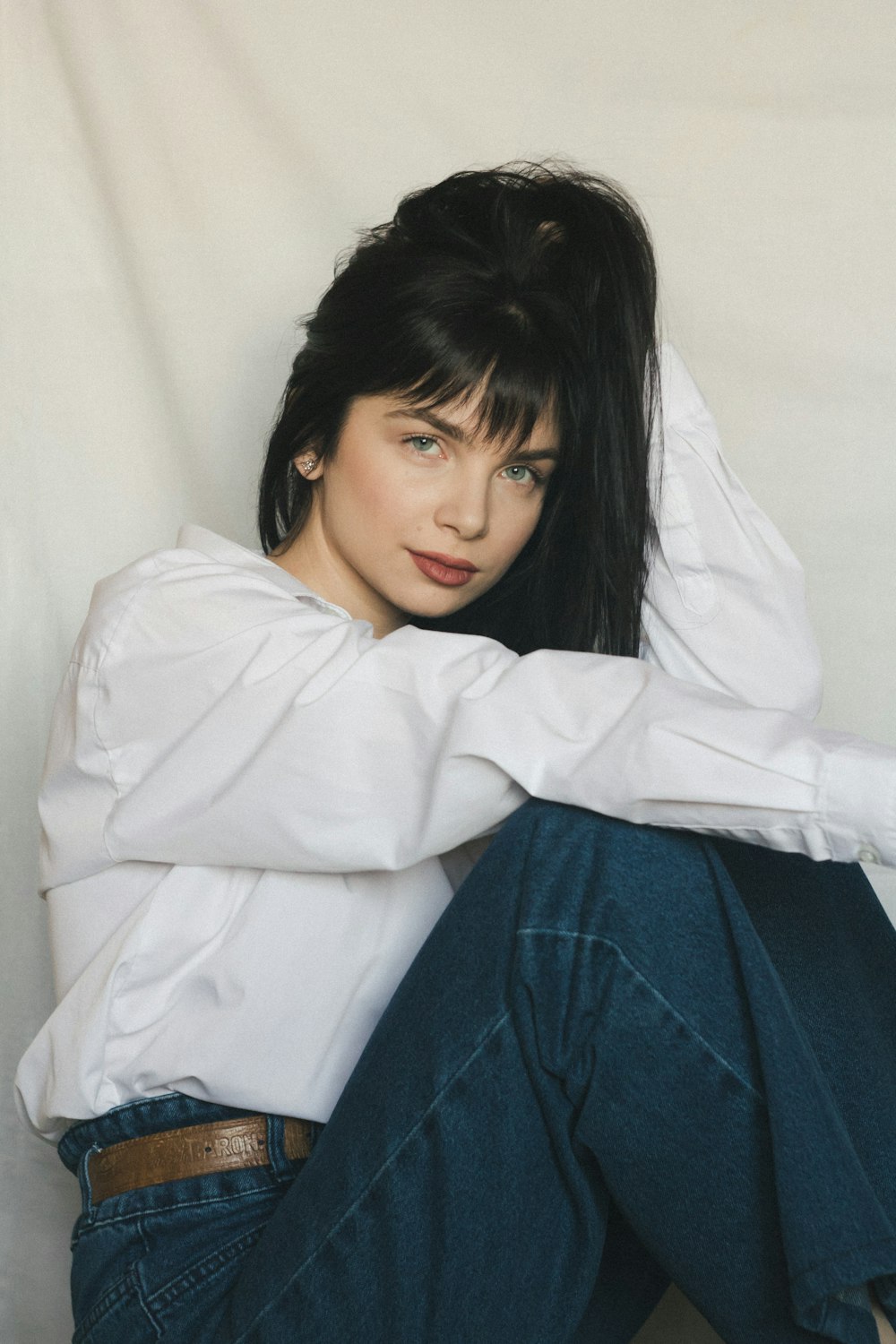 a woman sitting on the ground wearing a white shirt and jeans