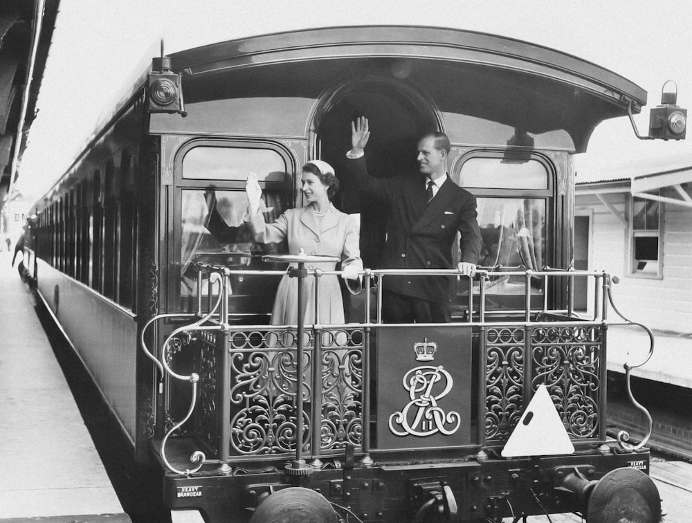 a black and white photo of people waving from a train