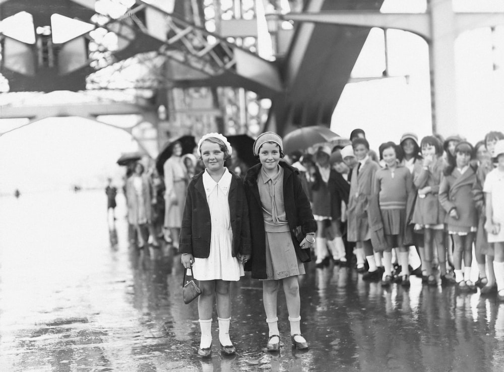 a black and white photo of two girls standing in front of a group of children