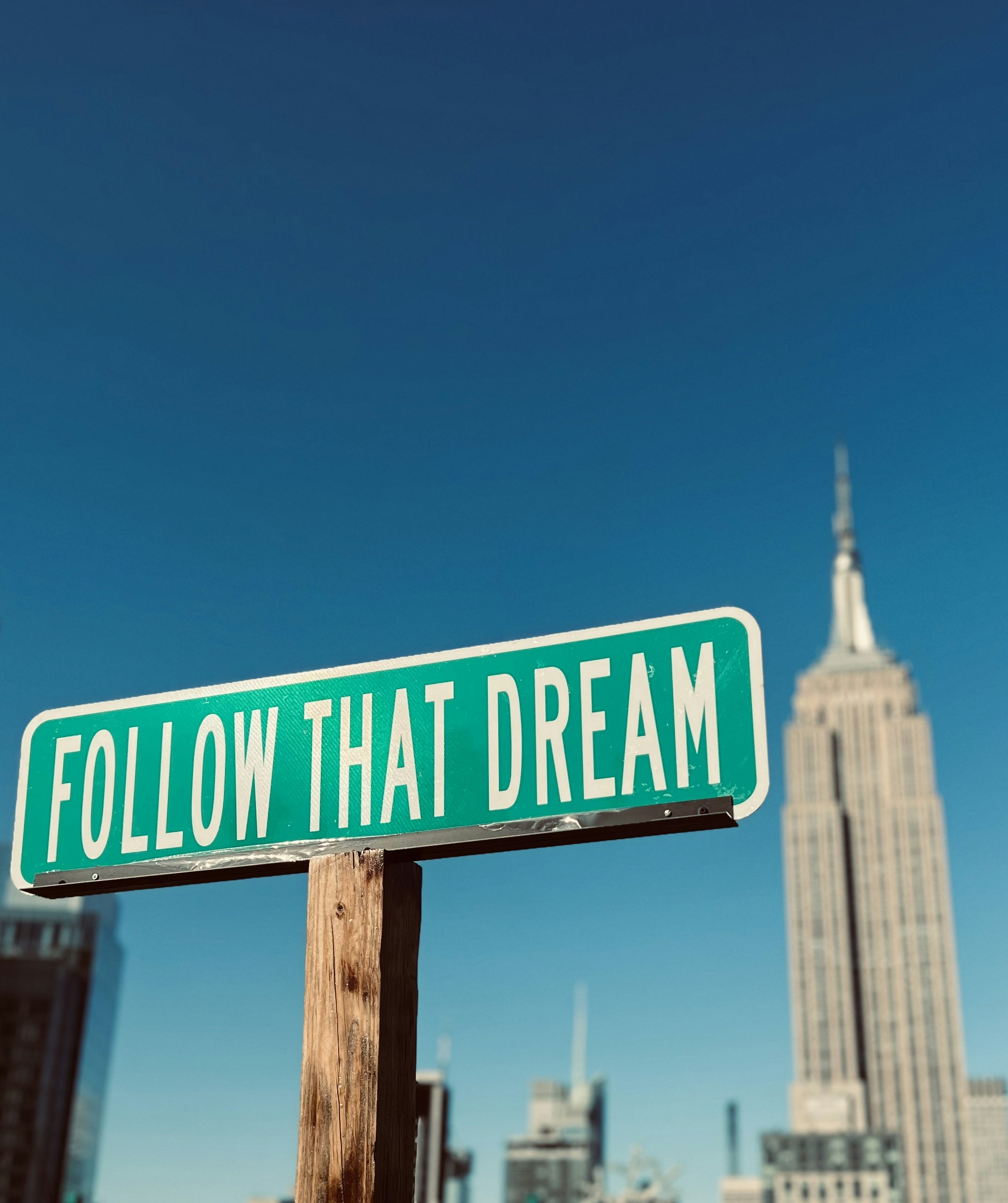 a green and white street sign that says follow that dream