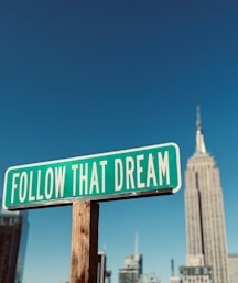 a green and white street sign that says follow that dream